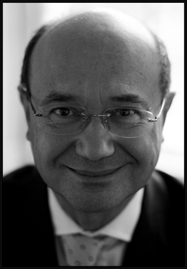 A black and white photo of a bald man with glasses.