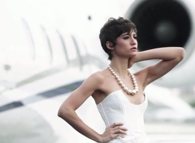 A woman in a white dress posing in front of an airplane.