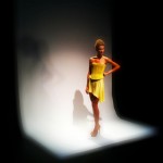 A woman in a yellow dress posing on a runway.