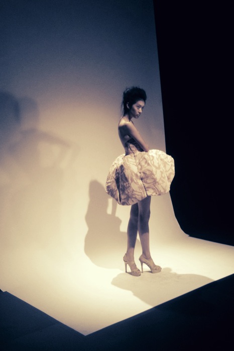 A woman in a white dress posing in a studio.