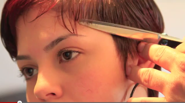 A woman cutting her hair with a pair of scissors.