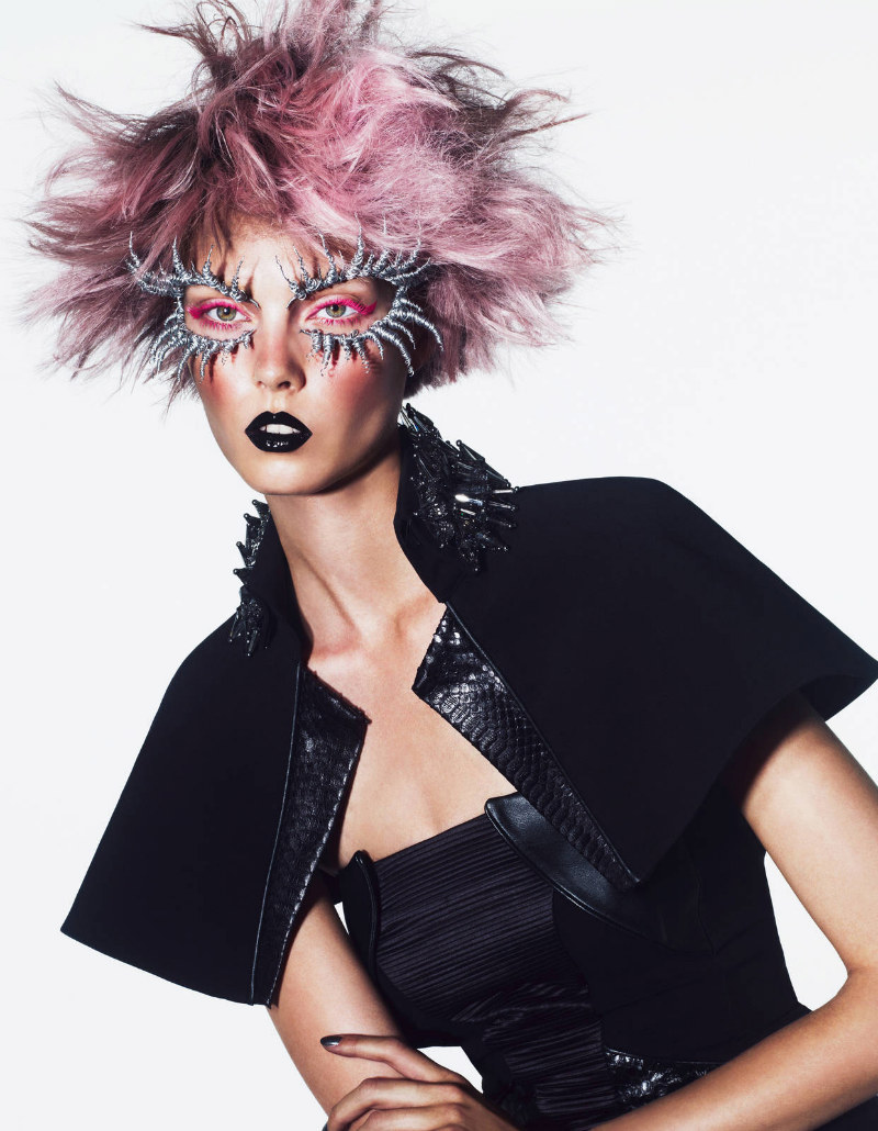 A woman with pink hair and black makeup is posing for a magazine.