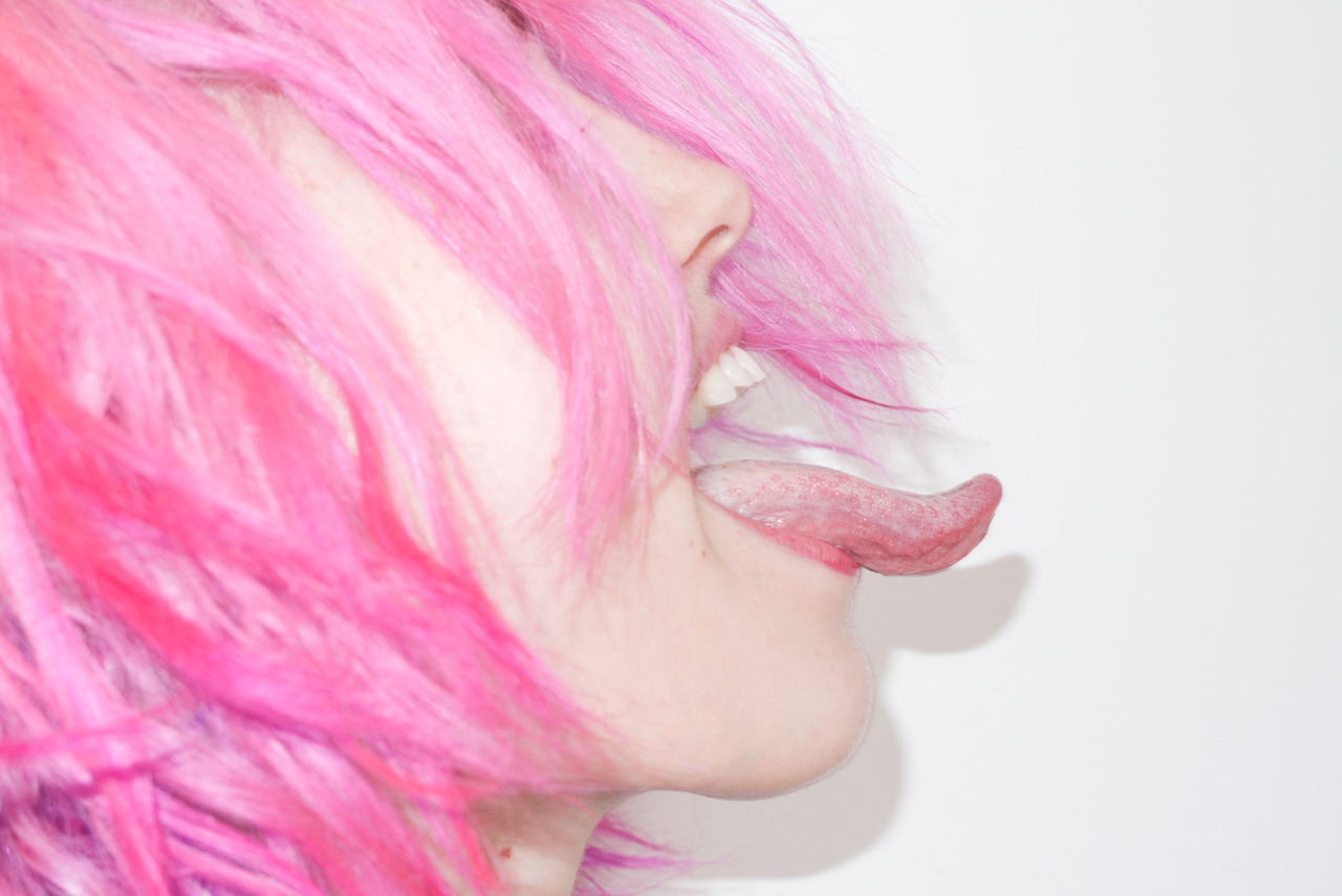 A girl with pink hair is licking her tongue.