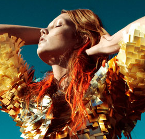 A woman with orange hair is posing in front of a blue sky.