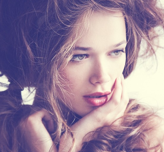 A woman with curly hair posing with her hand on her face.