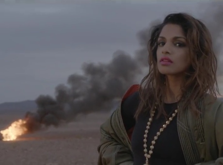 A woman standing in front of a fire in the desert.