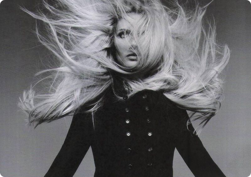 A black and white photo of a woman with long hair blowing in the wind.