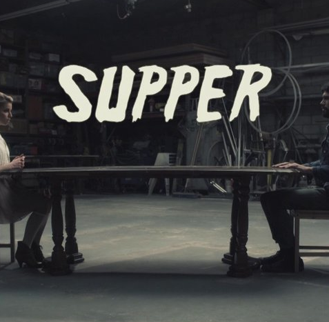 Two people sitting at a table with the word supper written on it.