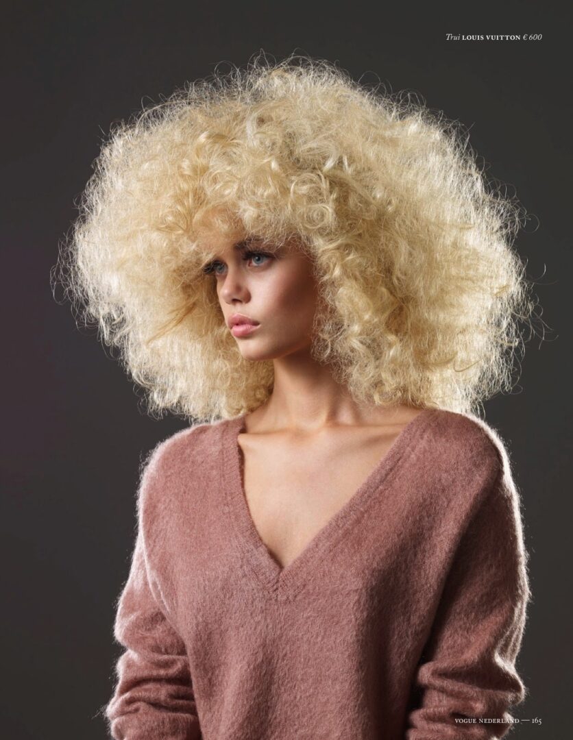 A woman with a big blond wig is posing for a magazine.