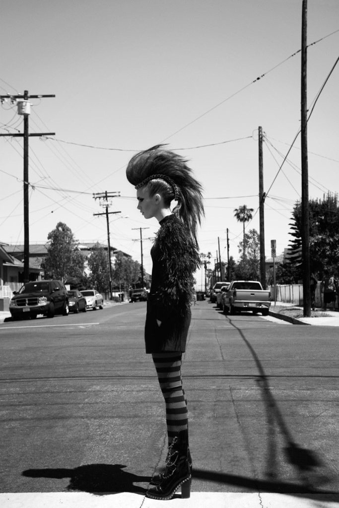 A black and white photo of a woman standing on a street corner.