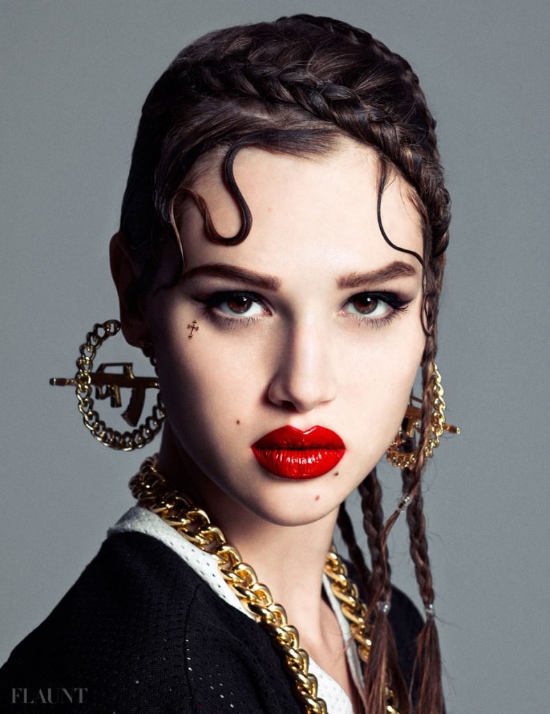 A woman with red lipstick and gold earrings posing for a magazine.