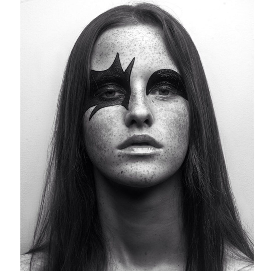 A black and white photo of a woman with black paint on her face.