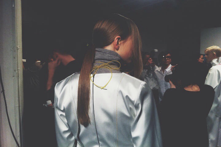 The back of a woman in a white coat with a ponytail.