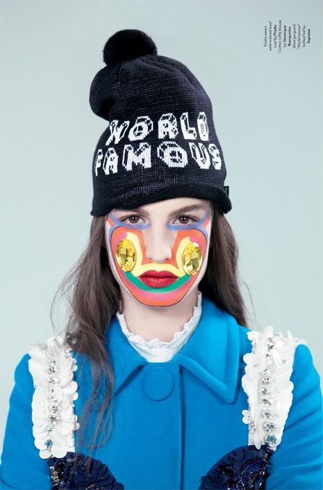 A woman wearing a hat with a colorful face painted on it.