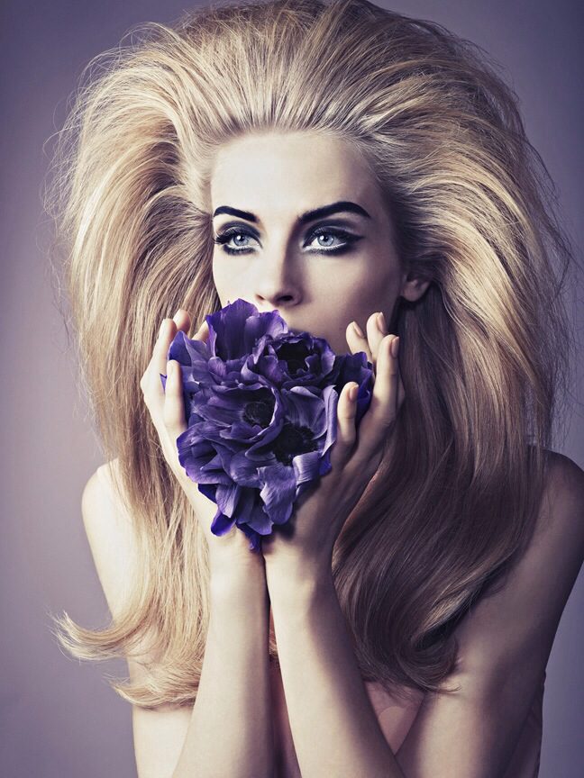 A woman with long blonde hair holding a purple flower.