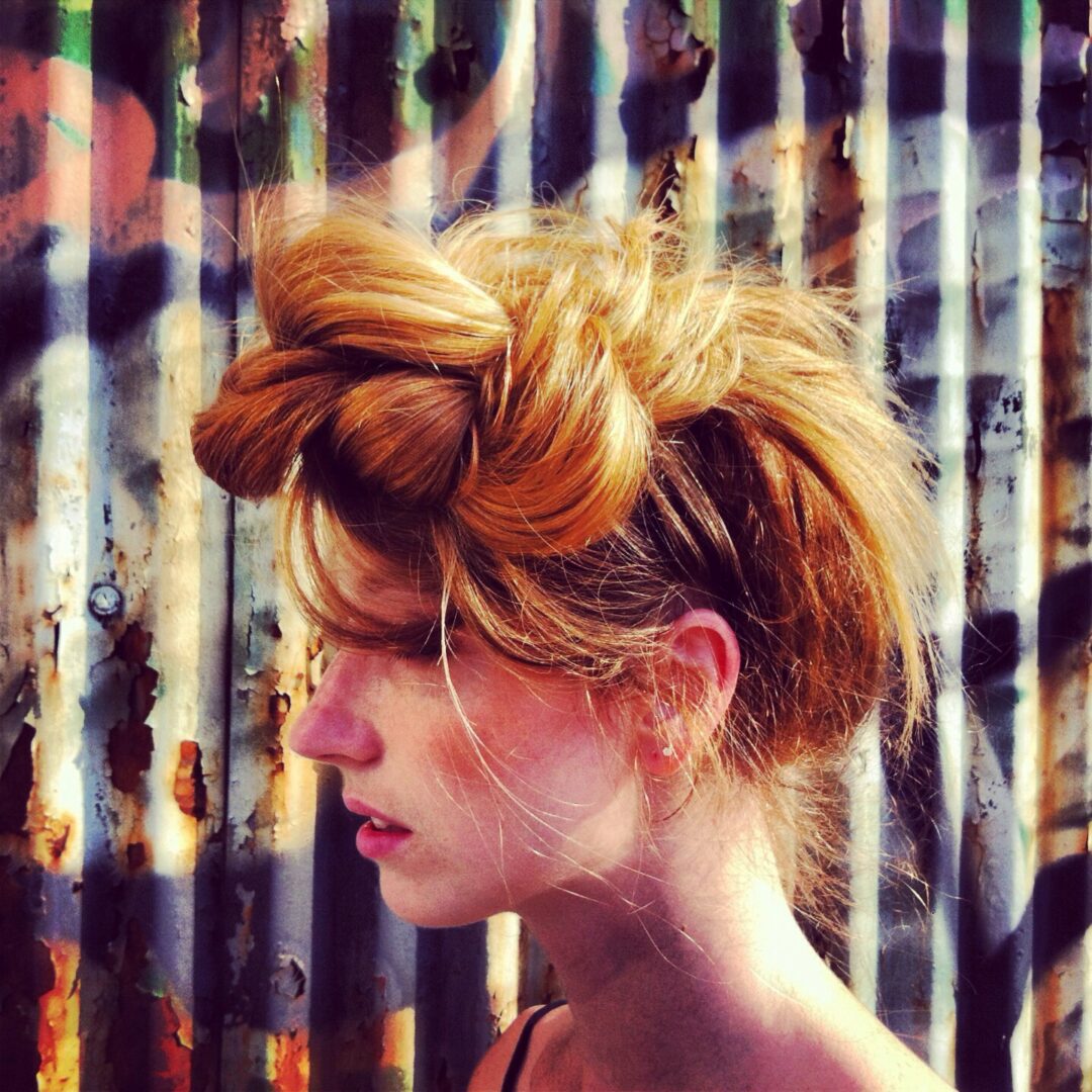 A woman with long hair standing in front of a rusty metal wall.