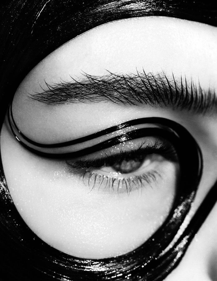 A black and white photo of a woman's eye with a black mask.