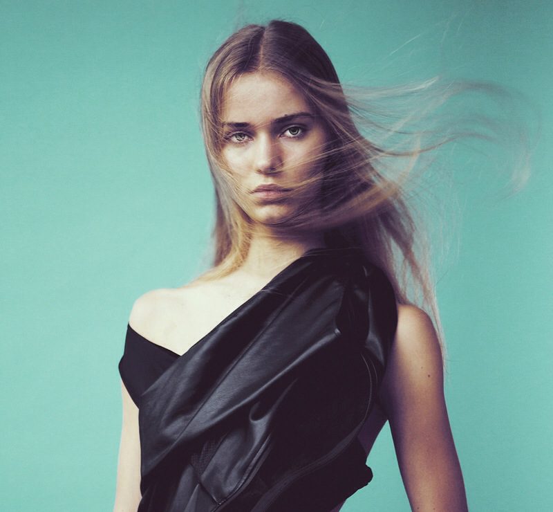 A woman in a black dress with her hair blowing in the wind.