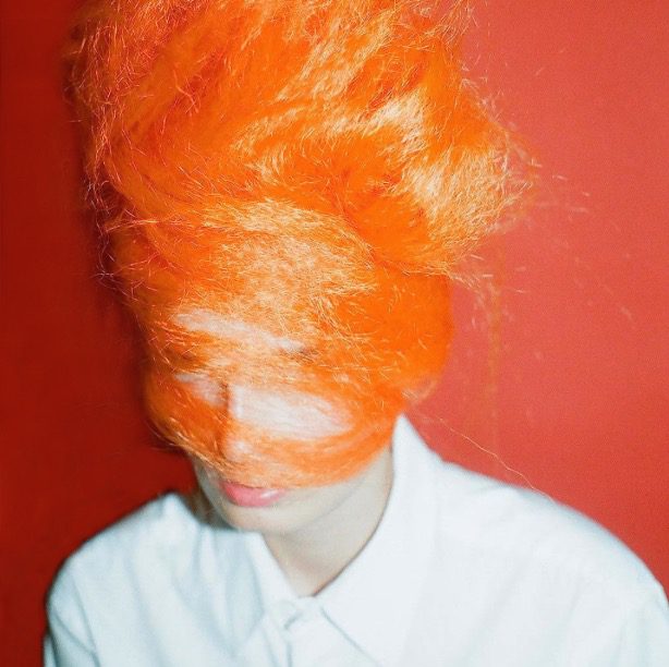 A woman with orange hair in front of a red wall.