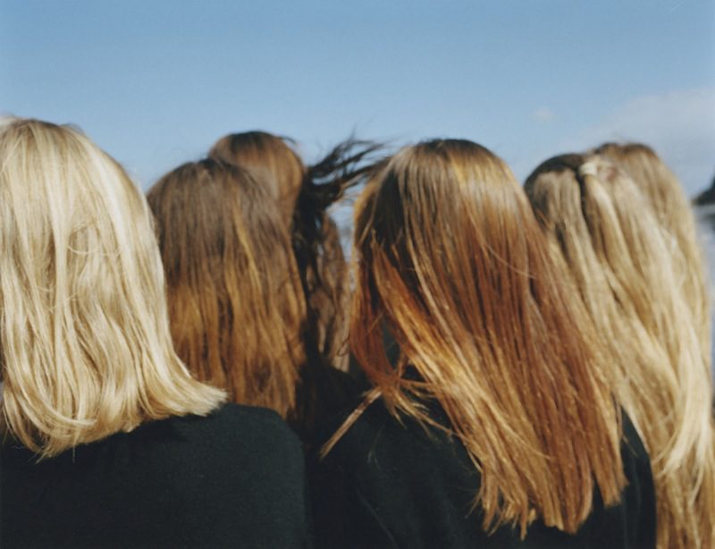 A group of women with long blonde hair standing in front of a body of water.