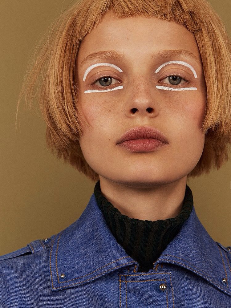 A woman in a denim jacket with eyeliner on her face.