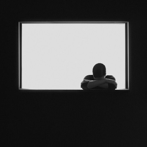 A black and white photo of a man looking out of a window.