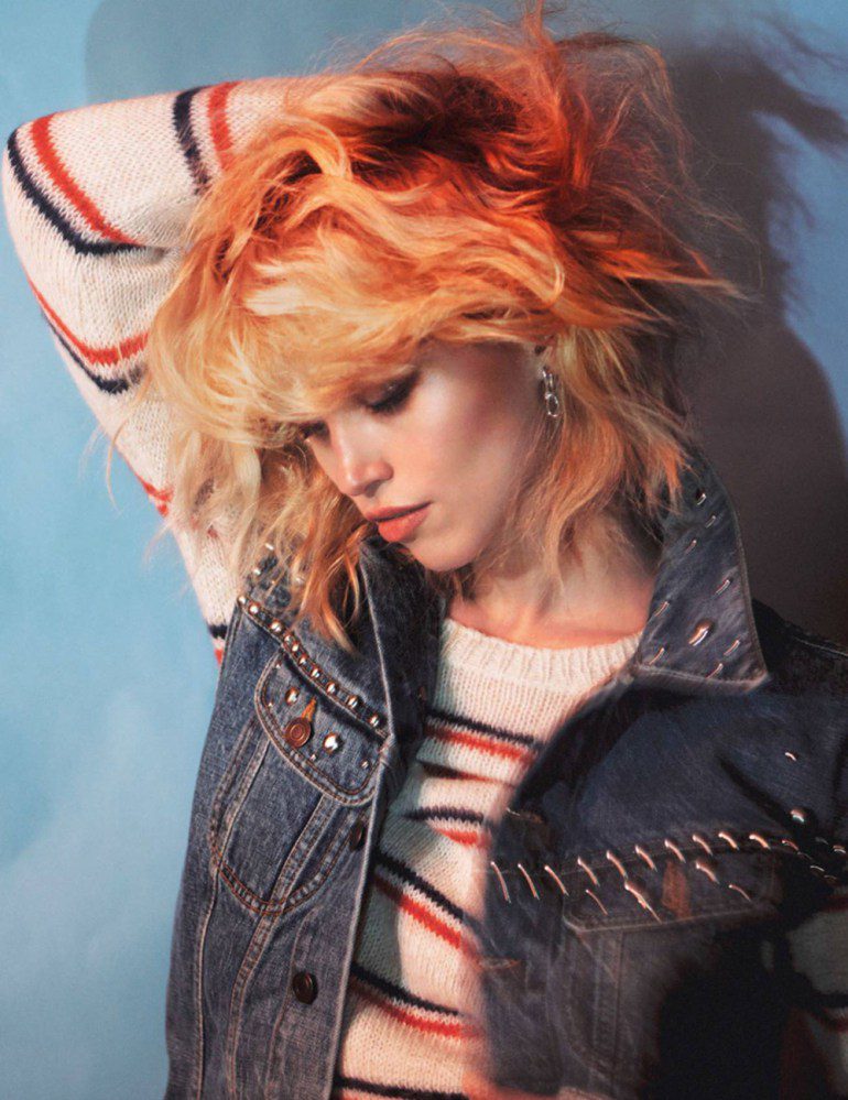 A woman with orange hair in a denim vest posing.