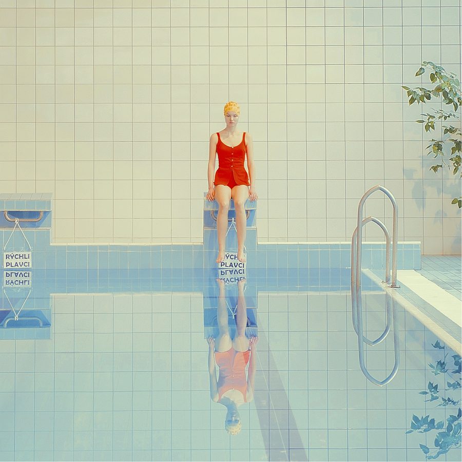 A woman in a red swimsuit sits on the edge of a swimming pool.