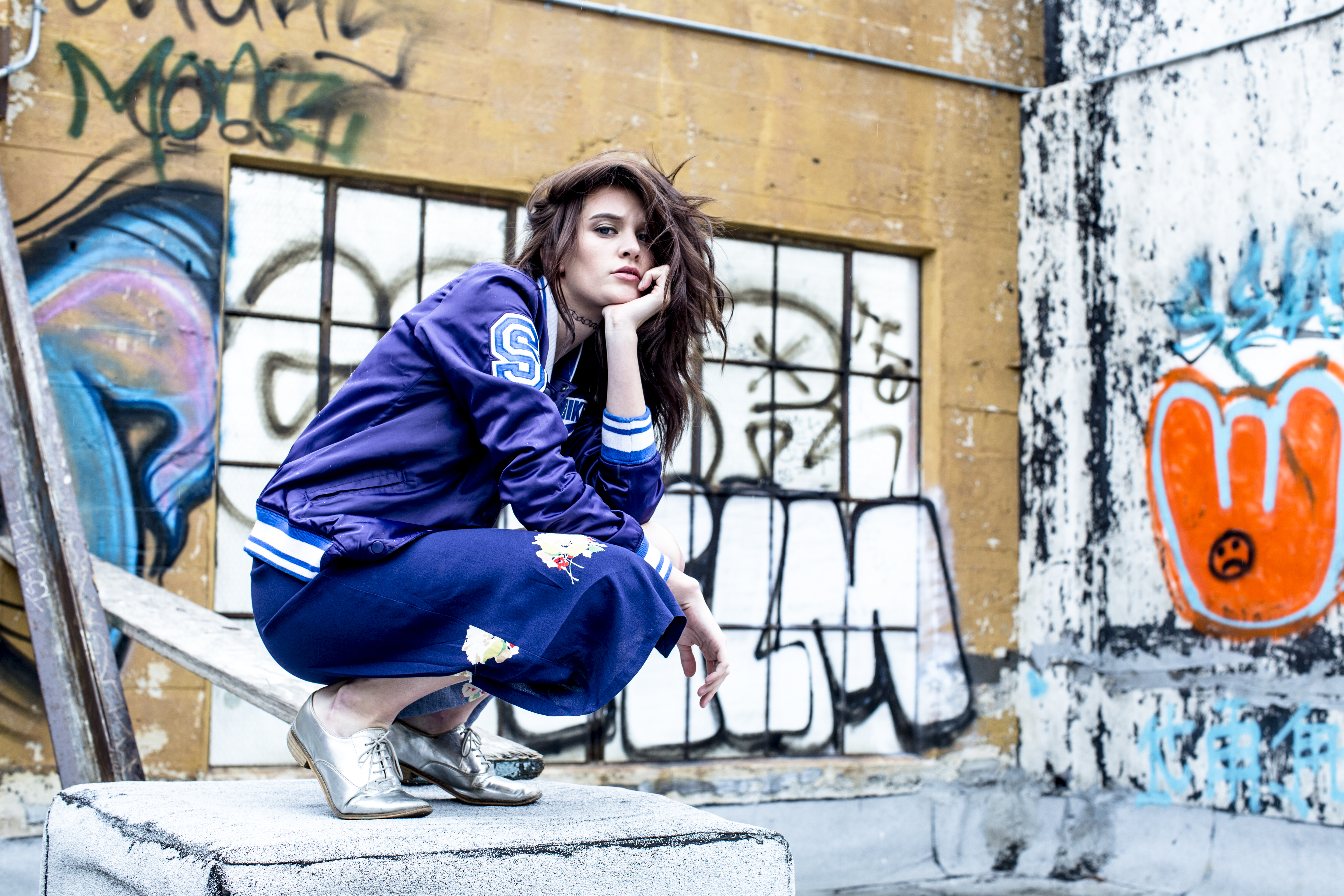 Young woman in blue jacket and skirt crouches on rooftop.