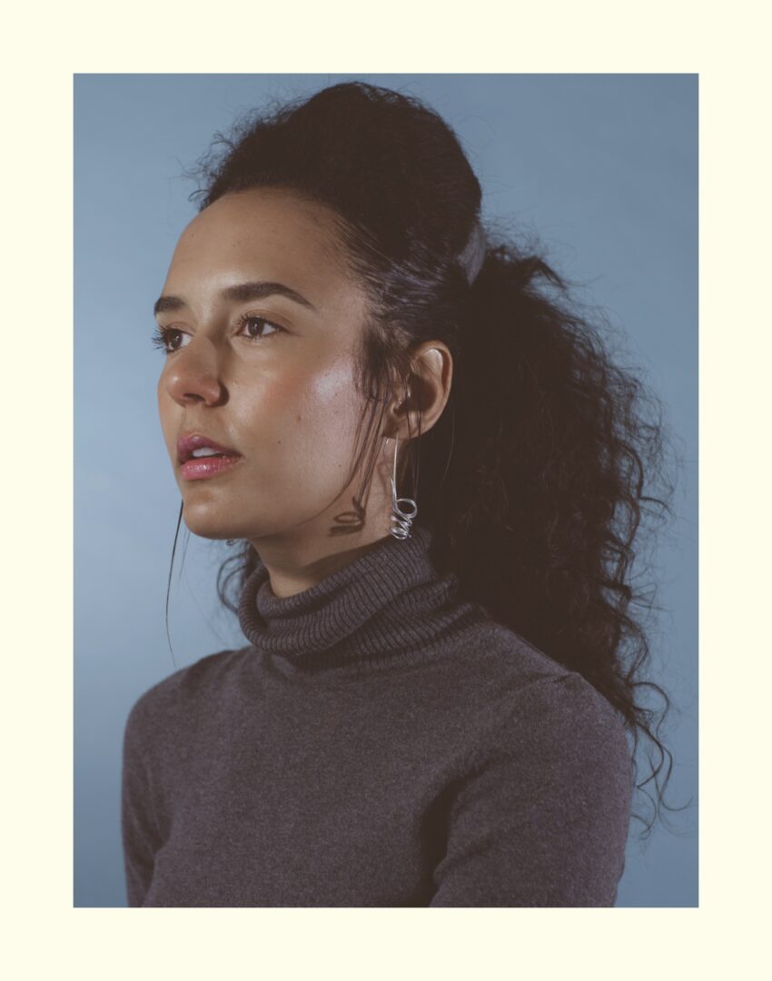 A young woman with curly hair and a turtle neck sweater.