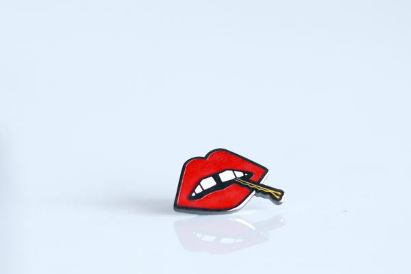 A "Lips" enamel lapel pin by LH™ with a mouth on it.