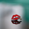 A "Lips" enamel lapel pin by LH™ on a glass surface.