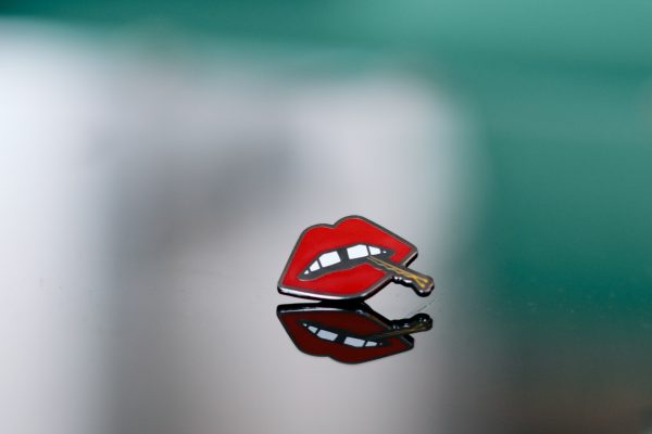 A "Lips" enamel lapel pin by LH™ on a glass surface.