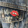 A "Lips" enamel lapel pin by LH™ with a red lipstick on it in the pocket of someone's jeans.