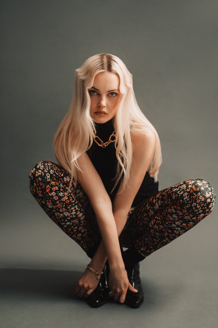 A blonde woman crouching in floral pants.