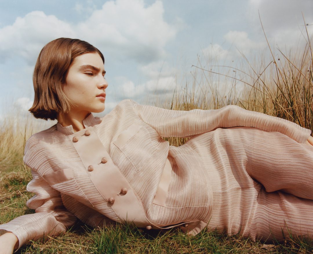 Model wearing a pink silk suit lying in a field.